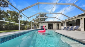 A swimming pool with a pink flamingo float, surrounded by a covered area with lounge chairs and a glass roof. - Pool Days, Sunshine & Memories for Everyone (Temple Terrace)