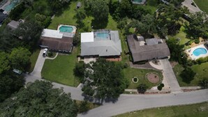An aerial view of a residential area with multiple houses, a swimming pool, and a well-maintained lawn. - Pool Days, Sunshine & Memories for Everyone (Temple Terrace)