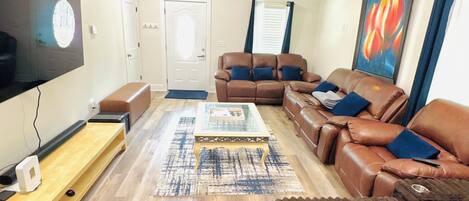 A living room with a flat-screen TV, a ceiling fan, a brown leather sofa set, and a wooden coffee table.
