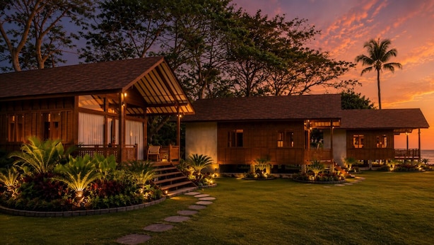 A beachfront property with a wooden house, a covered patio, and a well-lit garden at sunset. - Krisna Osea Villas  (Buleleng)