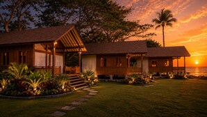 A beachfront property with multiple wooden structures, a well-maintained lawn, and a sunset view. - Krisna Osea Villas  (Buleleng)