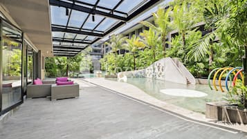 Un espace piscine intérieur moderne doté d’un plafond en verre, de coins salon confortables et d’un mur décoré d’une fresque.