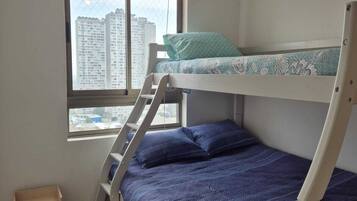 Dormitorio con literas, una ventana, un pequeño armario de madera y una lámpara en el techo.