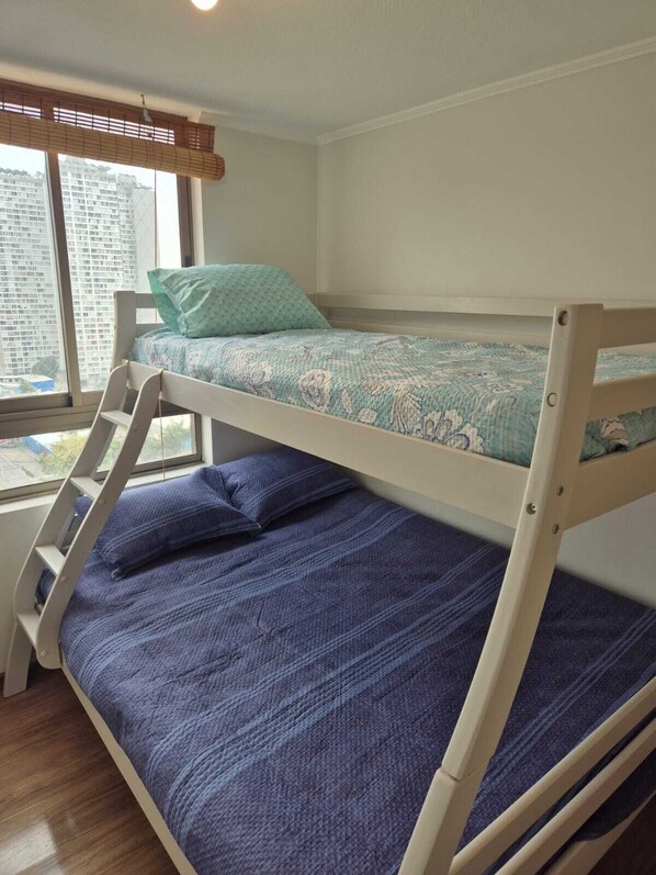 Una cama litera con escalera, una ventana con persianas y vistas a edificios.