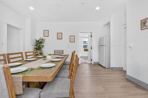 Uma sala de jantar moderna com uma mesa de madeira comprida, cadeiras estofadas cinzentas e um vaso com planta.