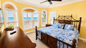 A bedroom with a bed, a desk, and a chair. There are windows with blinds, a ceiling fan, and a view of the ocean. - Ocean Front 6bed/6bath, gourmet kit, heated pool, private beach access (Ocean Isle Beach)