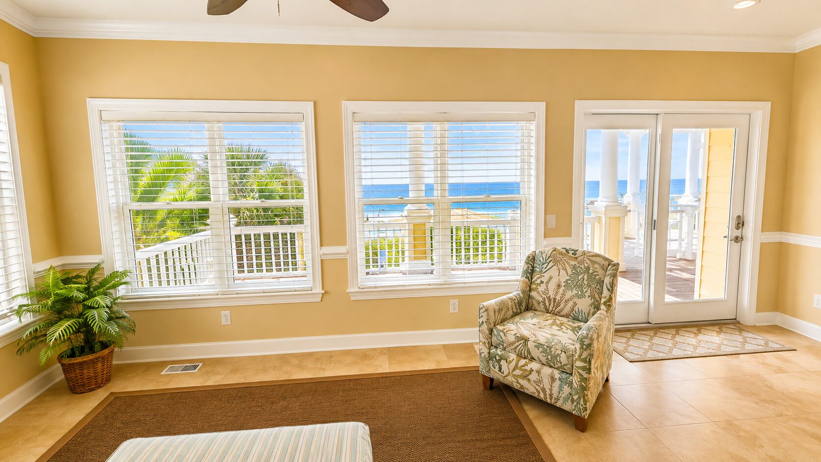 A room with a view of the ocean, a chair, a potted plant, and a door leading outside.