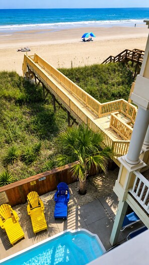 A wooden deck leading to a beach with a pool area and lounge chairs. - Ocean Front 6bed/6bath, gourmet kit, heated pool, private beach access (Ocean Isle Beach)