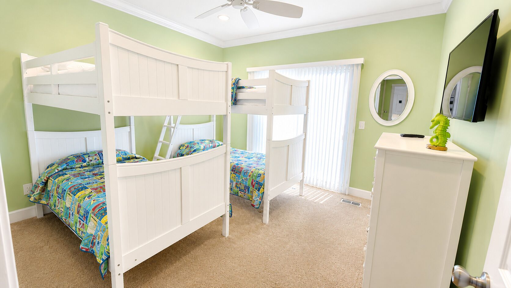 A room with bunk beds, a ceiling fan, a mirror, and a television.