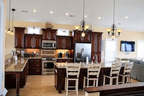 A modern kitchen with dark wood cabinets, stainless steel appliances, granite countertops, and a central island with bar stools. - Ocean Front 6bed/6bath, gourmet kit, heated pool, private beach access (Ocean Isle Beach)