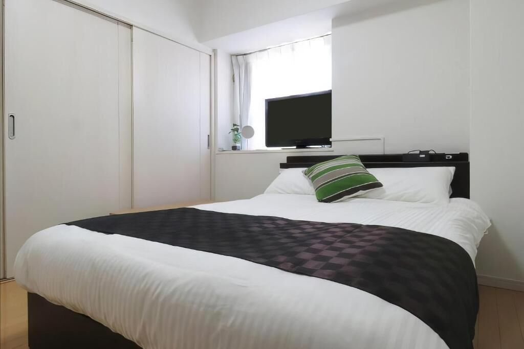 A bedroom with a bed, a television mounted on the wall, a window with curtains, and a wardrobe.