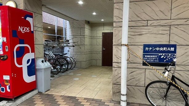 Un espacio público con una máquina expendedora roja, una bicicleta y un cartel que indica una ubicación.