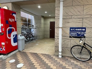 A public space with a red vending machine, a bicycle, and a sign indicating a location.