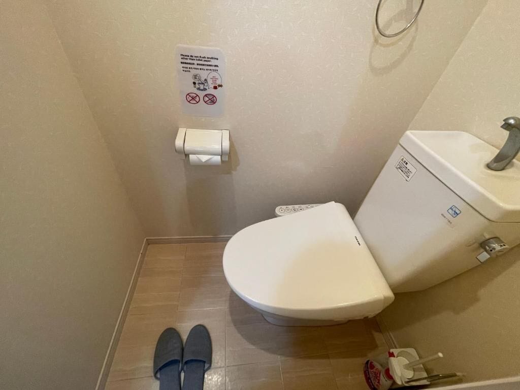 A small bathroom with a toilet, a hand dryer, and a sign on the wall.