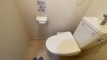 A small bathroom with a toilet, a hand dryer, and a sign on the wall.