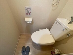 A small bathroom with a toilet, a hand dryer, and a sign on the wall.
