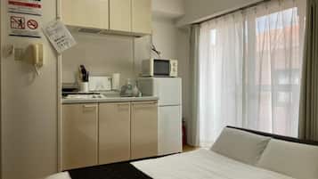A hotel room with a bed, a kitchenette, a microwave, and a window with curtains.