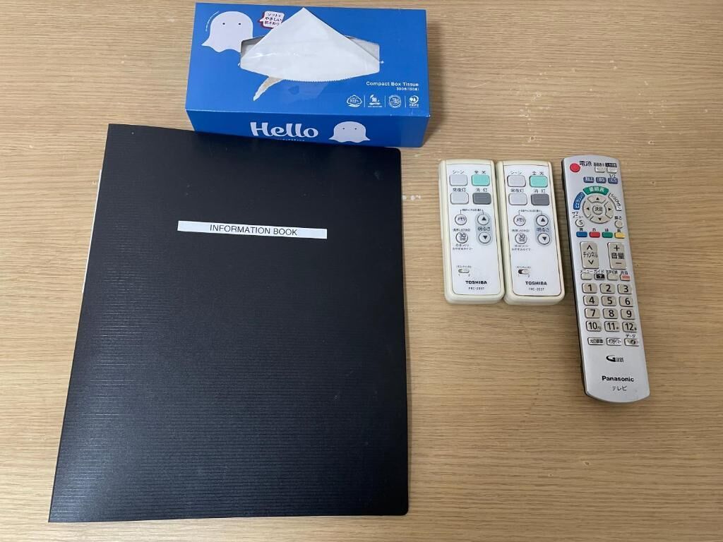 A black information book, a Hello tissue box, and two remote controls on a wooden surface.