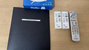 A black information book, a Hello tissue box, and two remote controls on a wooden surface.