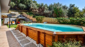 A rectangular swimming pool with a wooden deck surrounding it, set in a backyard with a wooden fence and greenery in the background. - Lovely home in Capezzano Pianore (Capezzano Pianore)