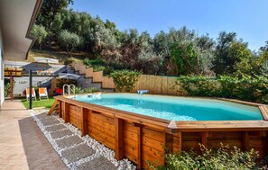 A rectangular swimming pool with a wooden deck surrounding it, set in a backyard with a wooden fence and greenery in the background. - Lovely home in Capezzano Pianore (Capezzano Pianore)