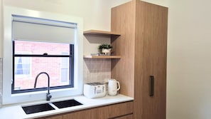A modern kitchen with a window, a sink, a countertop, a toaster, a kettle, and a wooden cabinet.