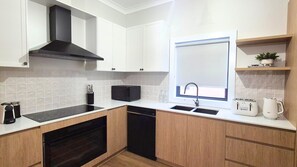 A compact kitchen with white cabinets, a black range hood, a built-in dishwasher, and a window above the sink.