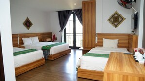 Quarto de hotel com duas camas, uma escrivaninha de madeira, um ventilador e uma janela com cortinas.