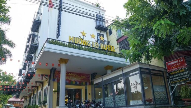 Um hotel com uma placa visível, entrada coberta e uma fileira de motocicletas estacionadas.