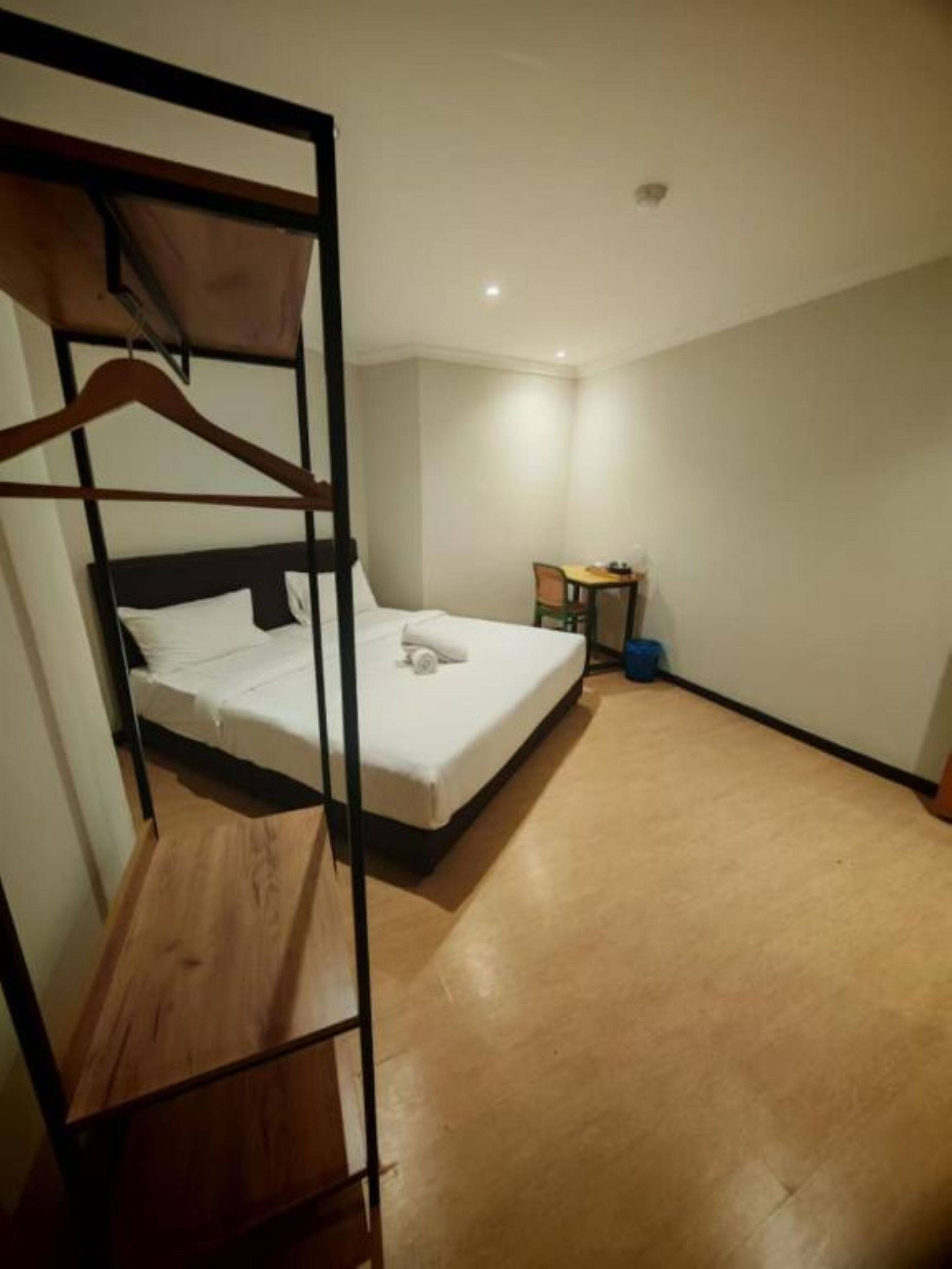 A single bed with a wooden frame and a mattress, a small table with a chair, and a blue trash bin.