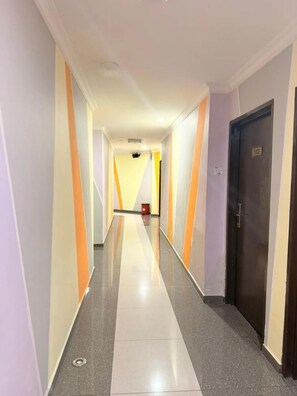 Un pasillo de hotel con suelo de baldosas, una puerta con placa de número y un cubo de basura.