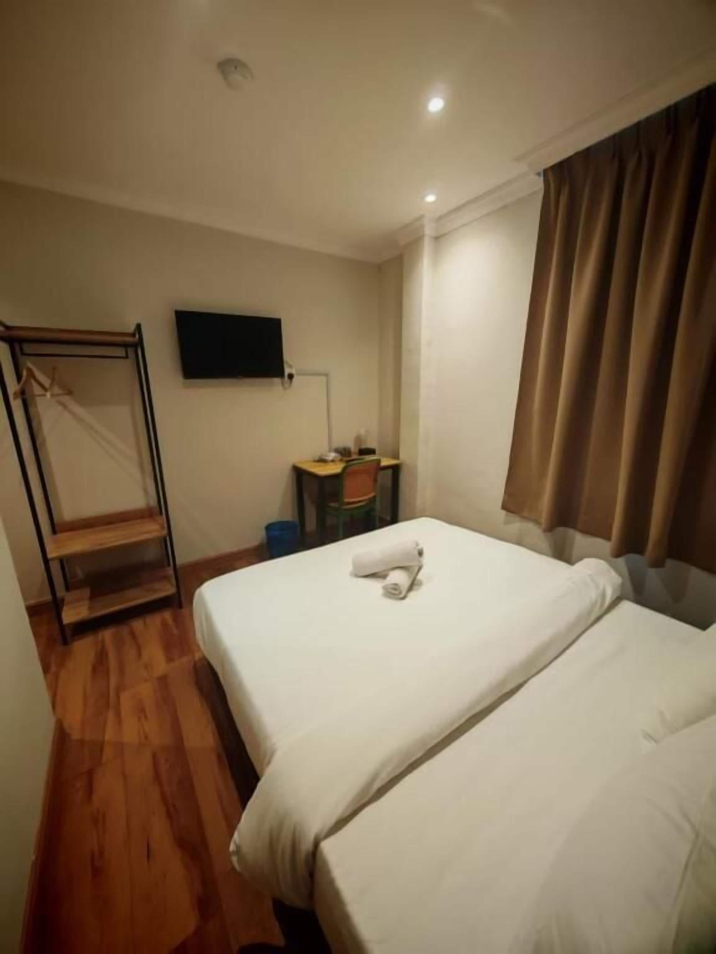 Habitación de hotel con cama, escritorio, silla, televisión y ventana con cortinas.