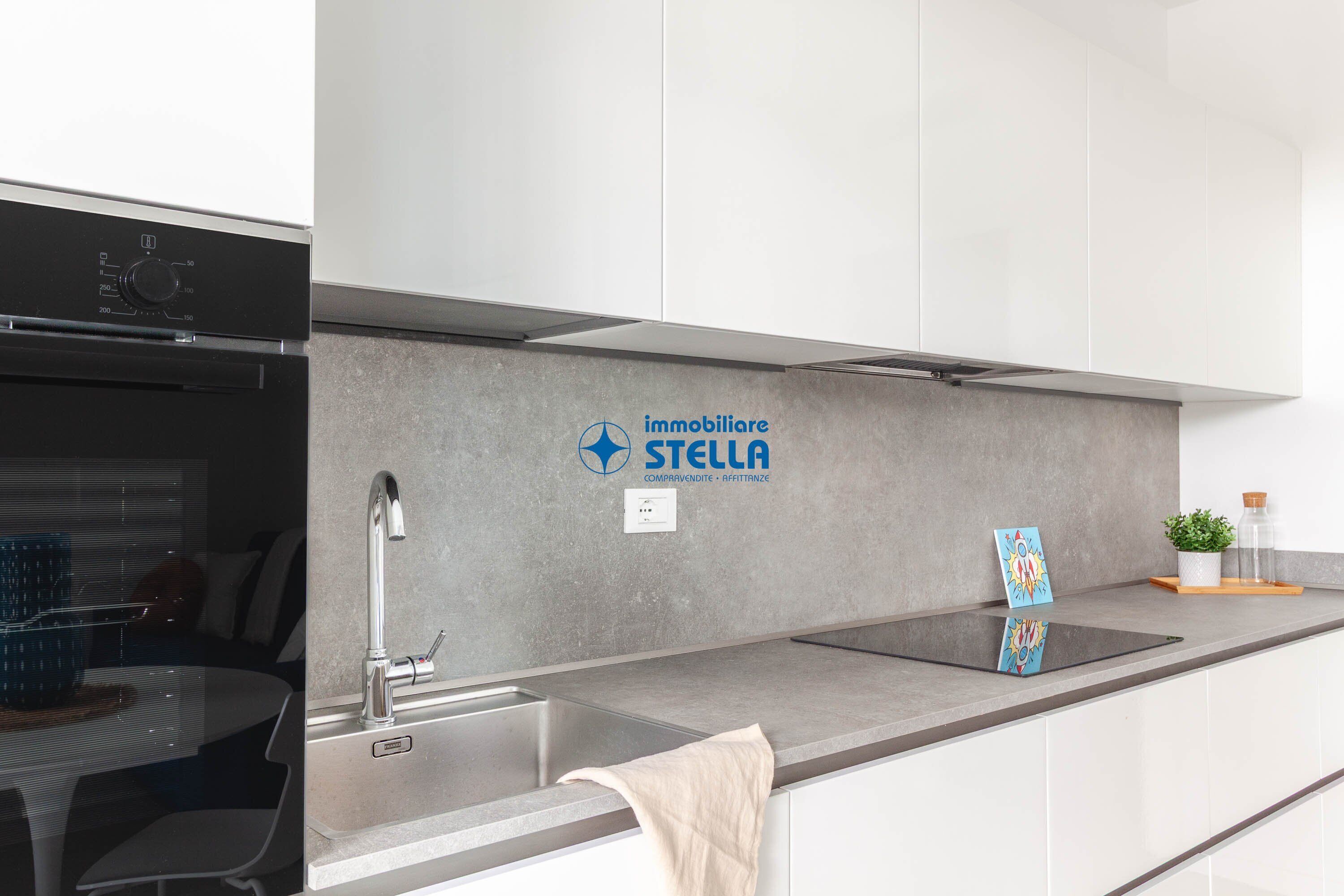 Een moderne keuken met een roestvrijstalen spoelbak, een ingebouwde oven en het logo van 'immobiliare STELLA' op de muur.