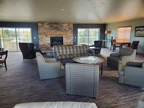 A spacious living area with a stone fireplace, comfortable seating, and large windows offering views of the outdoors.