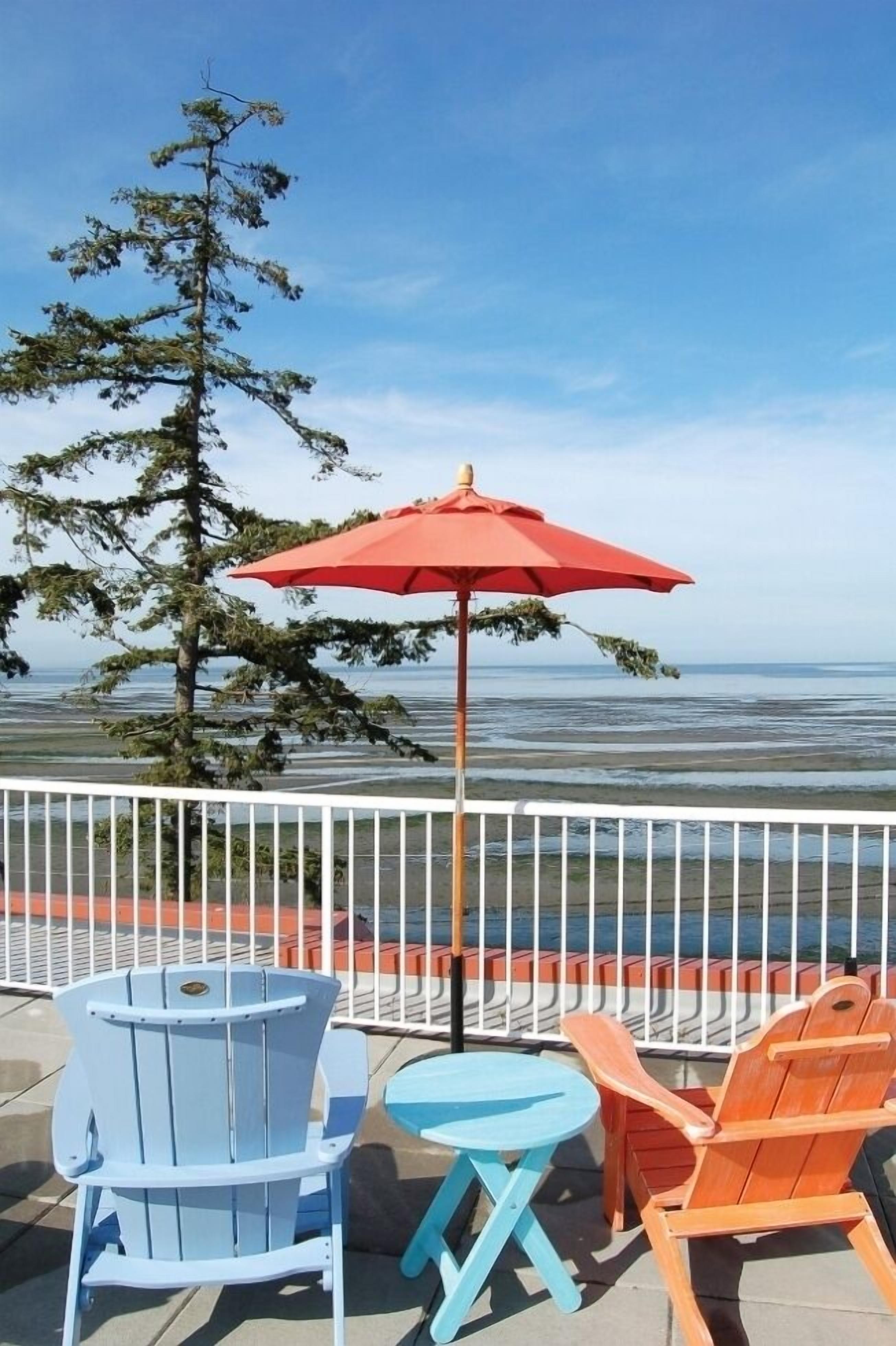 Une terrasse avec une table et des chaises, un parasol rouge et une vue sur l’océan.