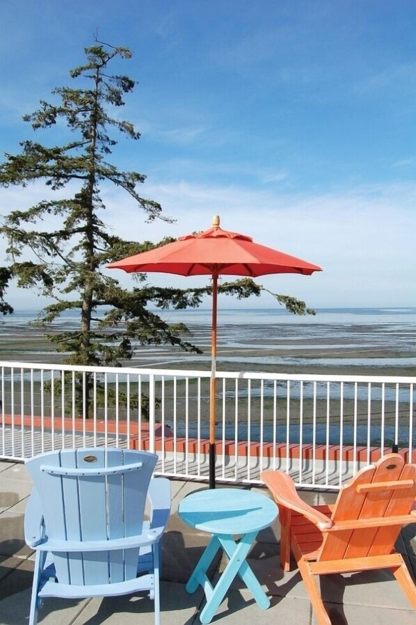 A patio with a table and chairs, a red umbrella, and a view of the ocean.
