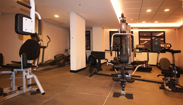 Une salle de sport équipée de divers appareils d’exercice, dotée d’un mur avec des miroirs et d’une fenêtre.