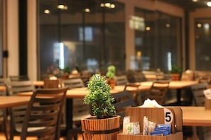 L’intérieur d’un restaurant avec des tables et des chaises en bois, ainsi qu’une petite plante en pot.
