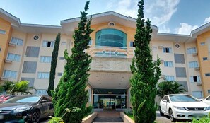 A multi-story hotel with a central entrance, surrounded by tall trees, and two cars parked in front. - Stylish Room for Rest & Relaxation | Outdoor Pool Access and Free Parking (Ponta Grossa)