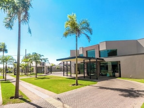 Un bâtiment moderne doté d’une entrée pavée, d’un espace extérieur aménagé avec des sièges et abrité, et de palmiers.