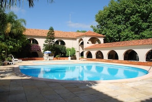 Une piscine dotée d’une terrasse carrelée, entourée d’un bâtiment orné d’arches et surmonté d’un toit en tuiles.