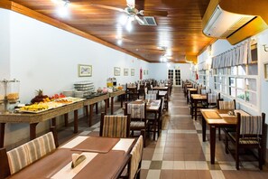 Ein großzügiger Speisebereich mit mehreren Tischen und Stühlen, ein Buffet mit verschiedenen Speisen und ein Deckenventilator.