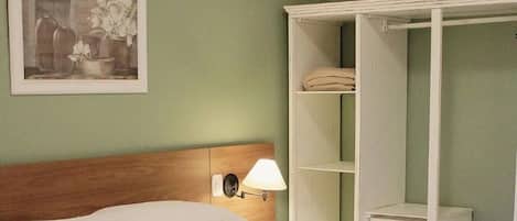 Habitación de hotel con cama, mesita de noche, lámpara, armario y un cuadro en la pared.