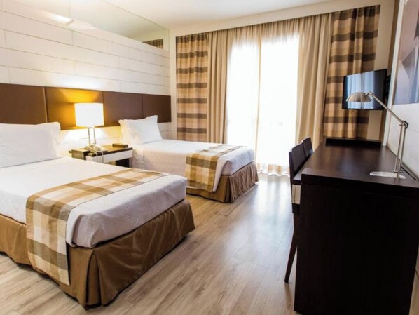 Habitación de hotel con dos camas, un escritorio, una silla, un televisor y una ventana con cortinas.