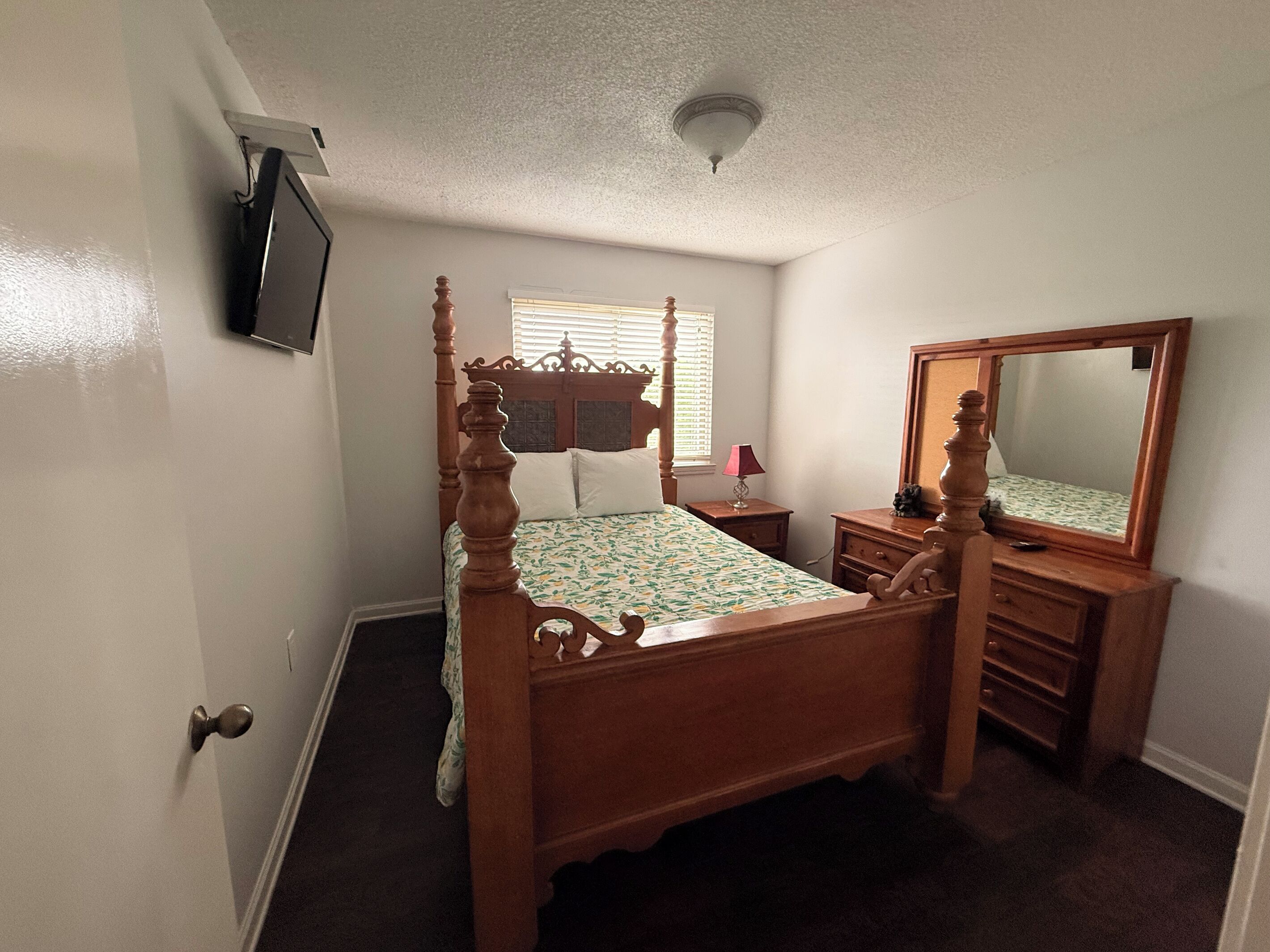 Una camera da letto con un letto a baldacchino, una cassettiera, uno specchio e una televisione montata a parete.