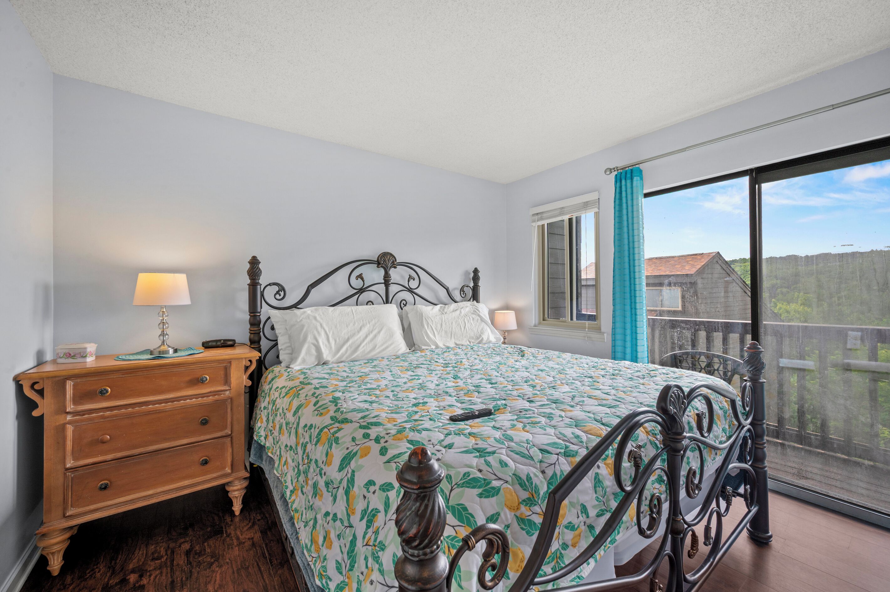 A bedroom with a bed, a dresser, a window with a view, and a balcony.