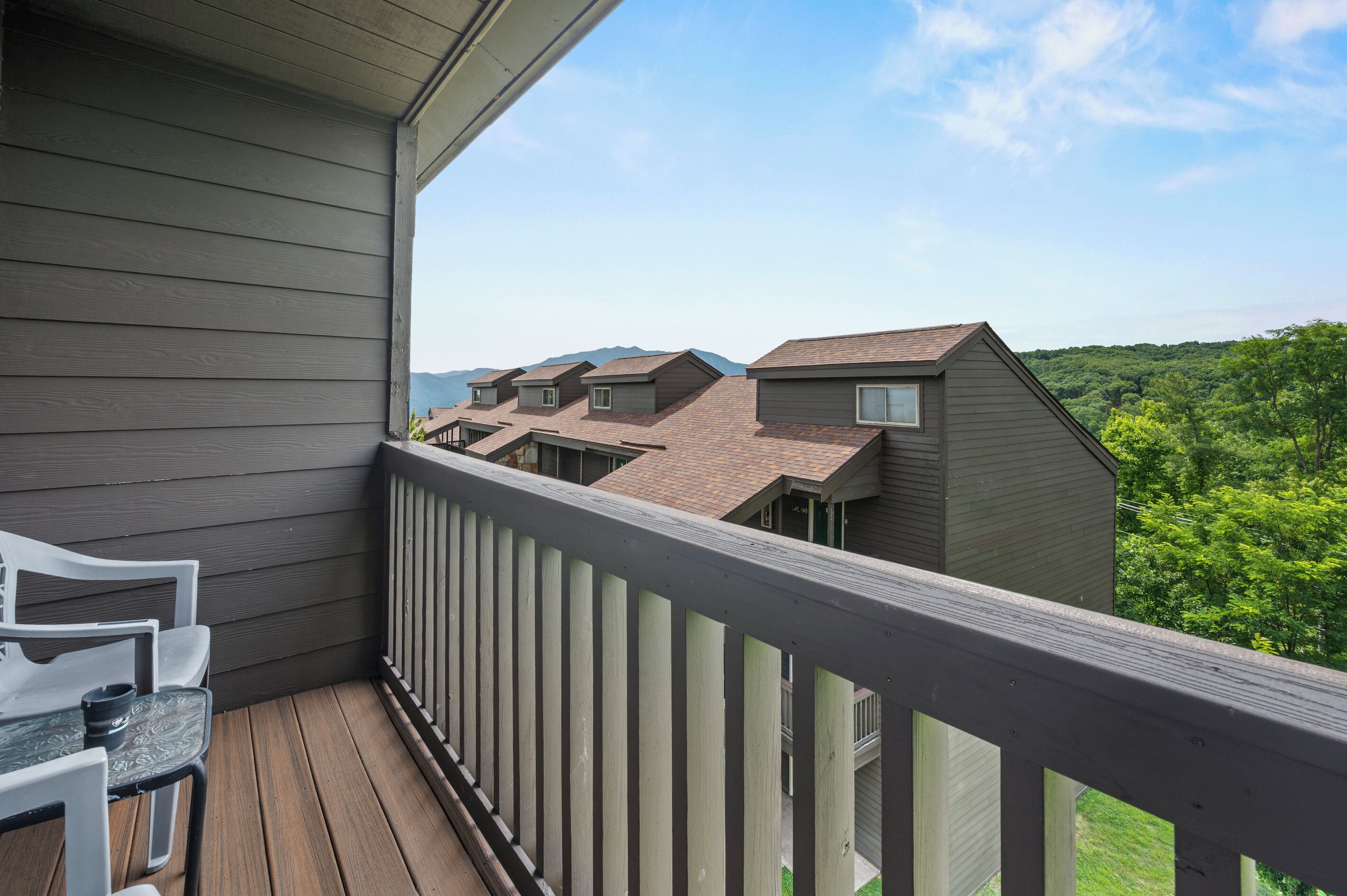 A balcony with a view of neighboring houses and a forested landscape.