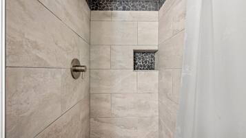A shower with beige tiles and a small stone accent wall.