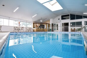 En inomhuspool med kaklade väggar, en bardisk och utsikt över staden genom stora fönster.