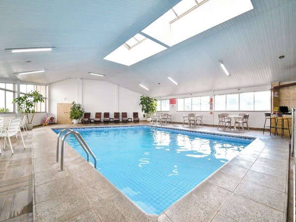 En inomhuspool med ett kaklat golv, en metallstege och en bar med stolar och en bardisk.